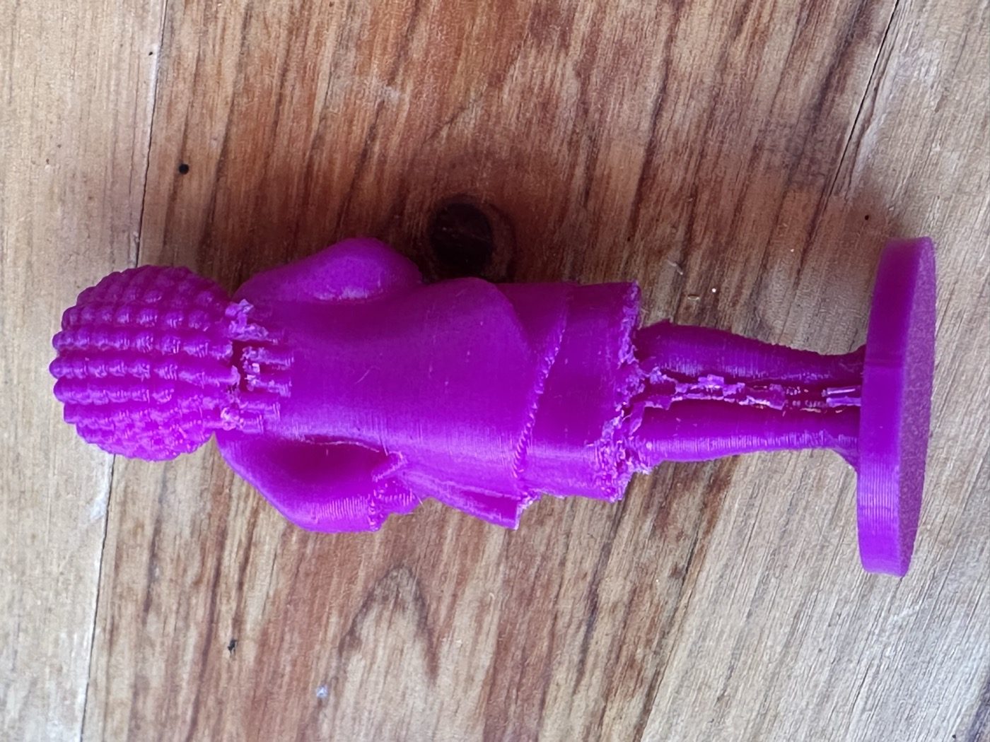 The printed 80 mm Amara figurine seen from behind: purple PLA, six short post stubs at the nape below the hair, rough support residue between the legs under the dress hem